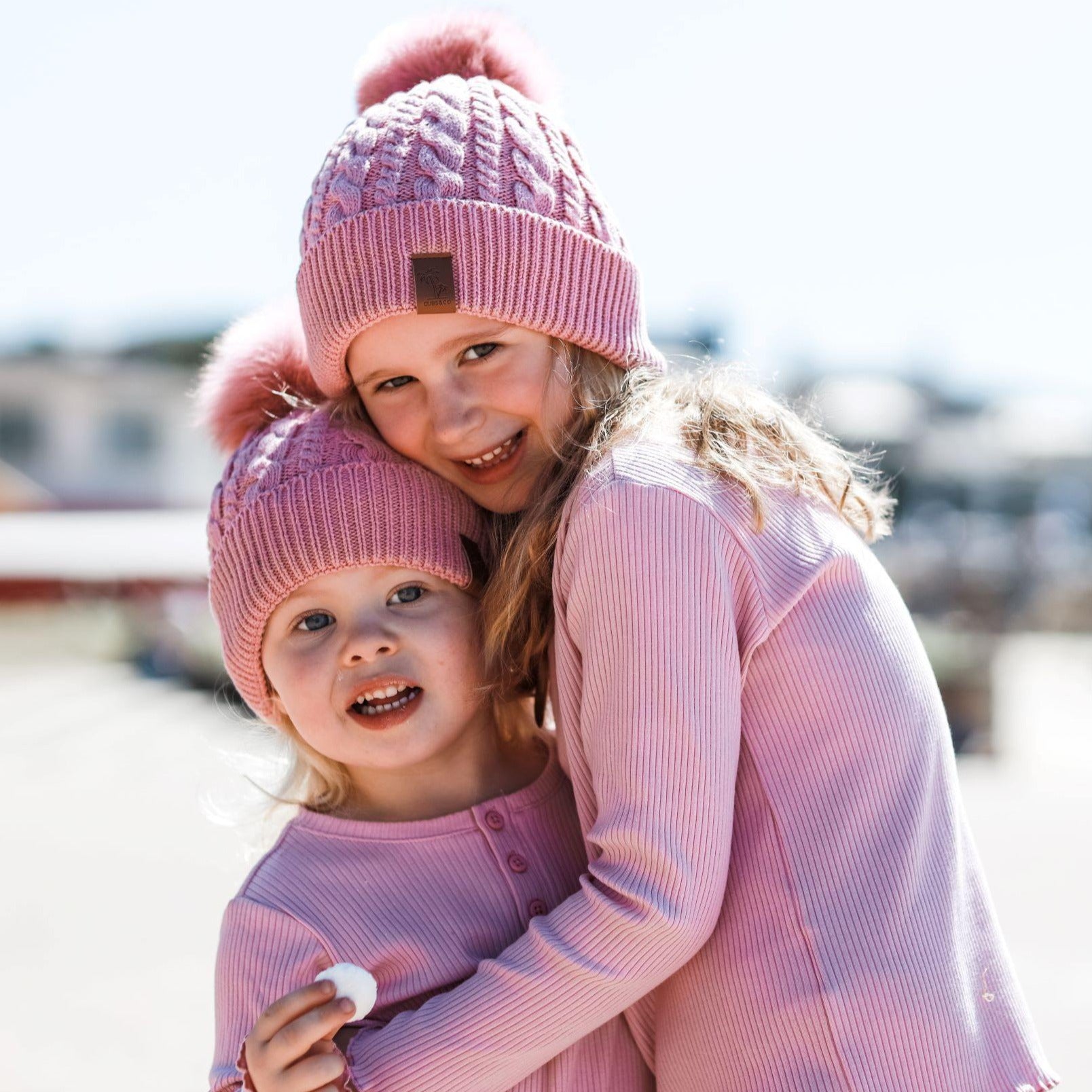 Sisters wearing pink winter cotton beanies with pom pom. Cubs & Co. Australia.