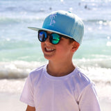 Boy wearing black kids sunglasses with UV400 protection at the beach. Cubs & Co. Australia